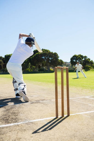 Home rear view of cricket player batting while playing on field against clear sky